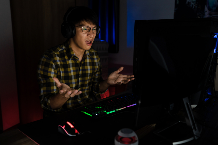 Азіатський чоловік-геймер у навушниках підкреслив комп'ютер