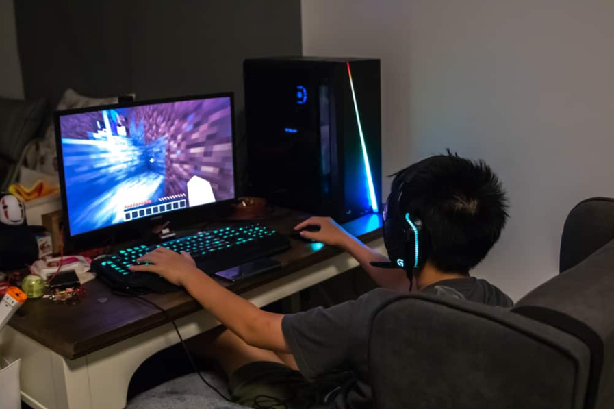 Азіатський хлопчик грає в Minecraft на комп’ютері з ігровим обладнанням і периферійними пристроями RGB