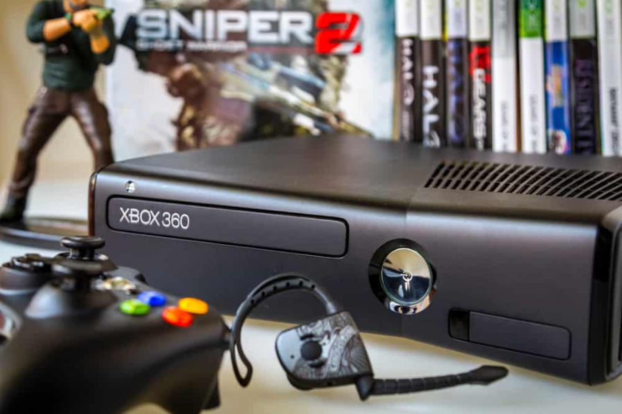 Чорна ігрова консоль Xbox 360 з контролером і фоновими іграми