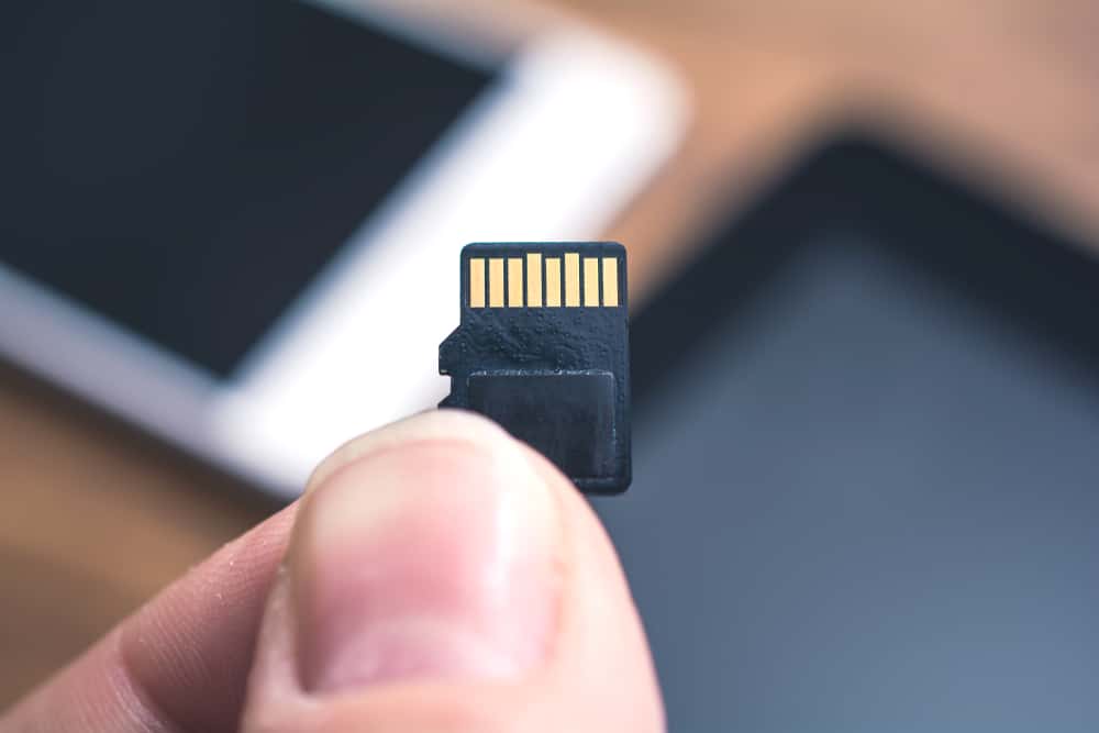 Чоловічі пальці, що тримають картку Micro SD із планшетом і смартфоном у фоновому режимі