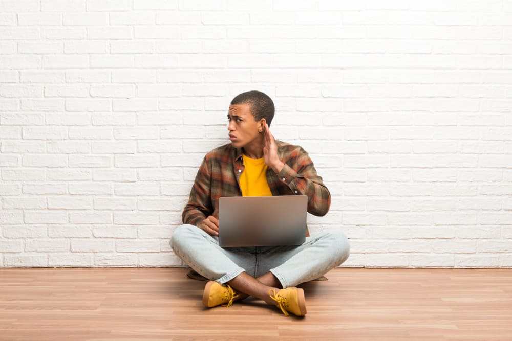 чоловік сидить на підлозі зі своїм ноутбуком і щось слухає