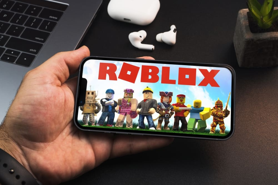Чоловік тримає смартфон із ігровим додатком Roblox на екрані на чорному тлі столу
