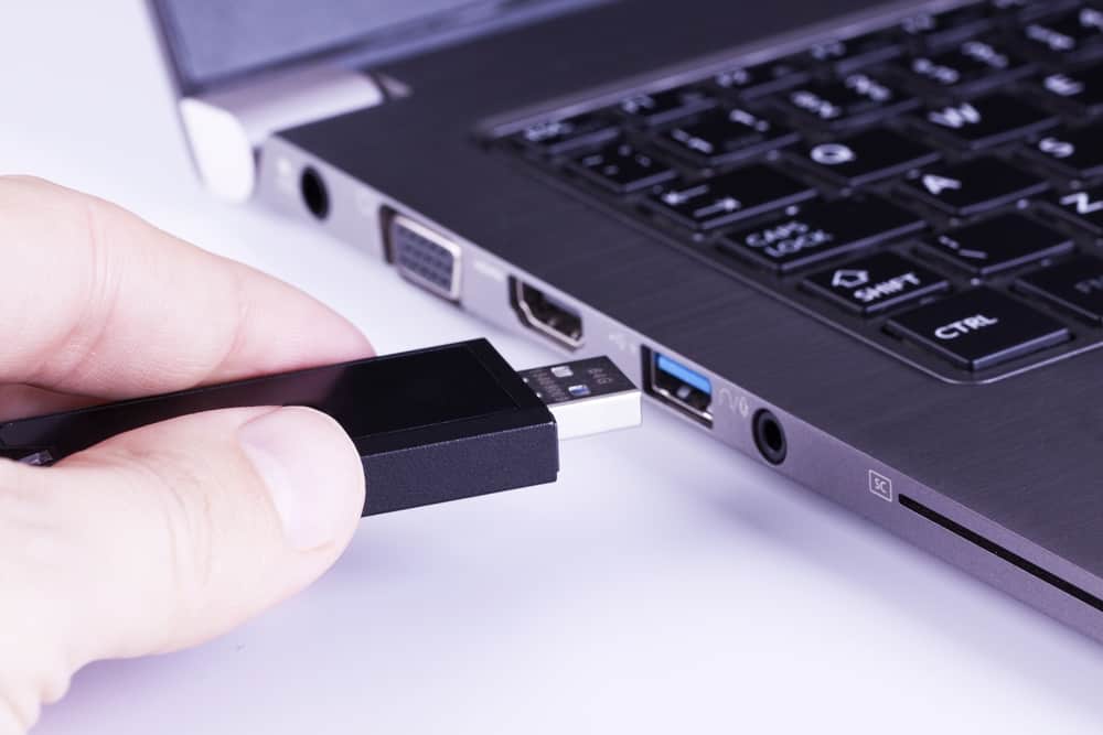 Чорний знімний флеш-пам'ять у пальцях із USB-слотом ноутбука на білому тлі
