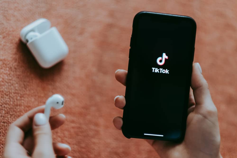 Дівчина тримає iPhone і AirPods із логотипом TikTok на екрані