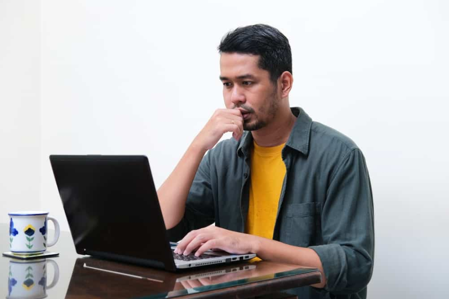 Дорослий азіатський чоловік показує мислення жестом перед своїм ноутбуком