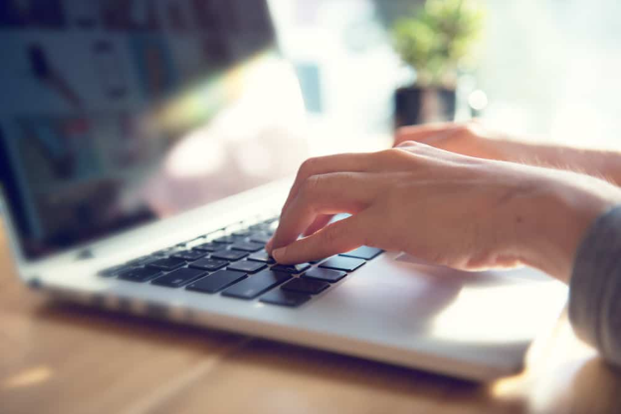 Жіночі руки крупним планом друкують на ноутбуці на дерев'яному столі з сонячним світлом