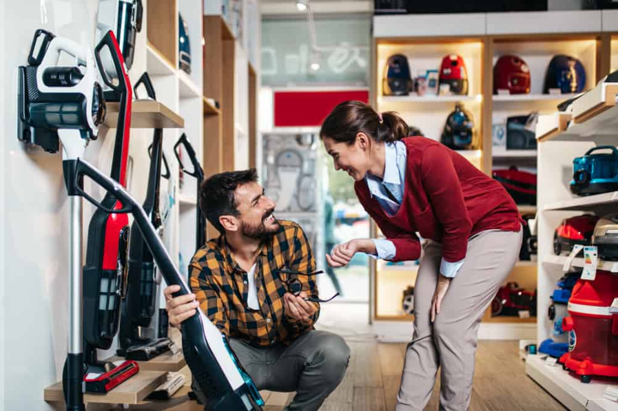 Молода пара, задоволені клієнти купують роботизований пилосос у магазині техніки.