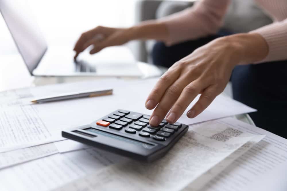 Крупним планом зосередитися на жіночих рук, роблячи розрахунки. Молода жінка переглядає паперові купюри, керує щомісячними витратами та доходами домогосподарства, використовуючи програму електронного банкінгу, планує інвестиції.