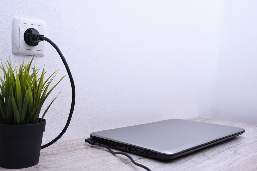 Ноутбук, комп'ютер заряджається від розетки 220 вольт на столі біля стіни. Енергія, накопичення