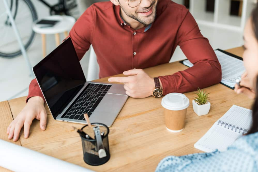 Обрізаний вид колег, які сидять за столом і використовують ноутбук