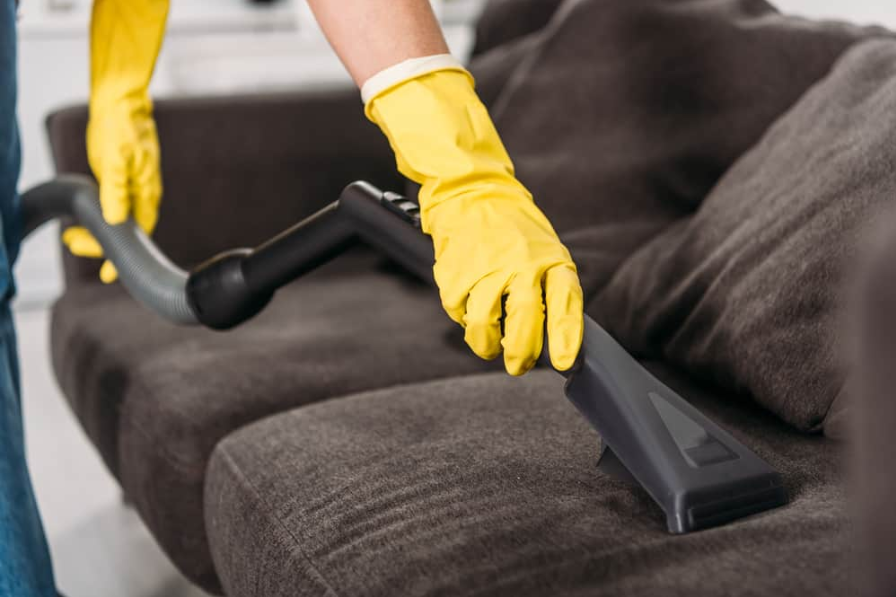 Обрізаний вид жінки в гумових рукавичках прибирає диван