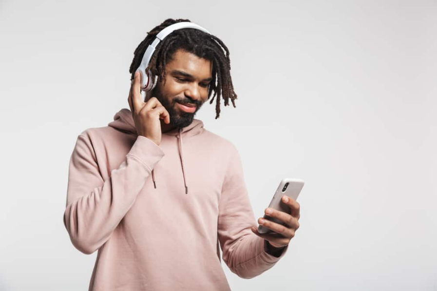 Портрет із задоволенням афроамериканця за допомогою мобільного телефону та бездротових навушників, ізольовані на білому тлі