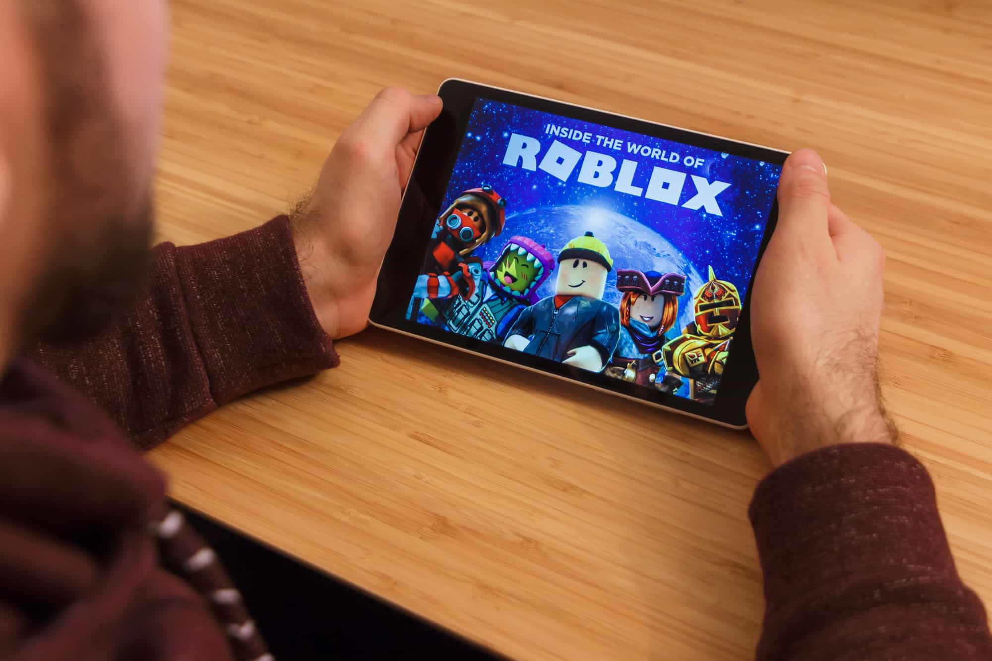 Чоловік тримає смартфон і грає в мобільну гру Roblox. Ілюстративне редакційне зображення на бамбуковому фоні