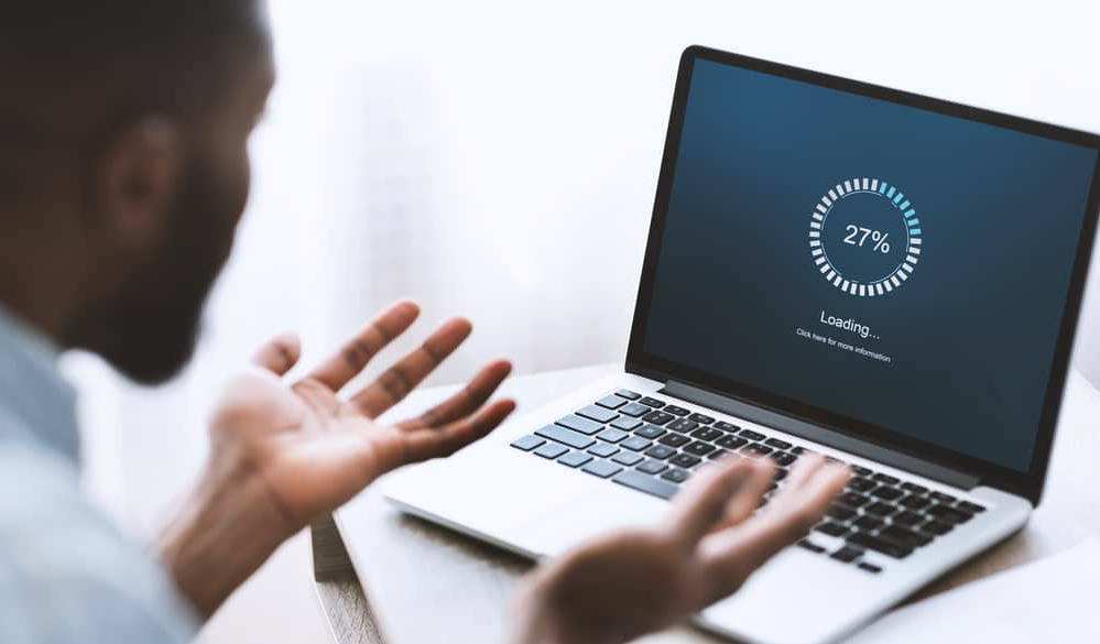 Стурбований афроамериканець дивиться на ноутбук із завантаженням