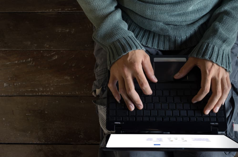 Вид зверху чоловічі руки за допомогою ноутбука, сидячи на дерев'яній підлозі