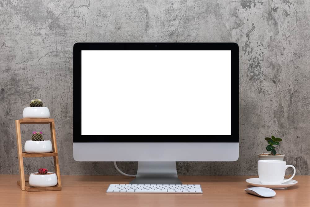 Все в одному комп’ютері, миші, клавіатурі, горщиках для кактусів, вазі для рослин і чашці кави на дерев’яному столі