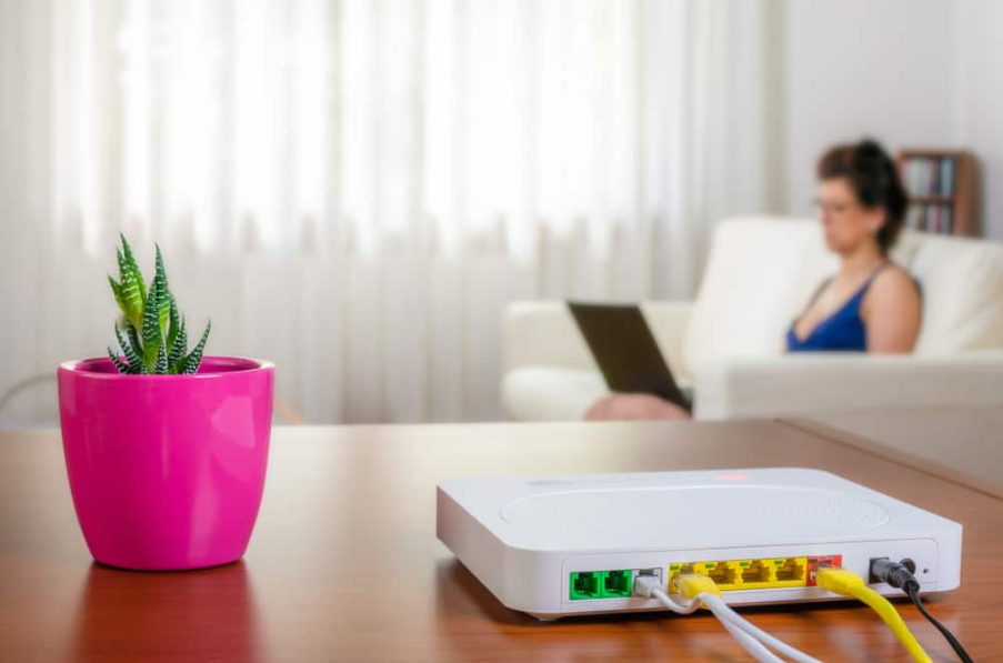 Крупним планом модемний маршрутизатор на столі у вітальні з жінкою, яка користується ноутбуком, сидячи на дивані