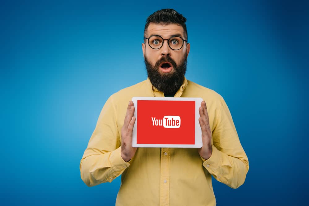 Здивований бородатий чоловік показує цифровий планшет із youtube